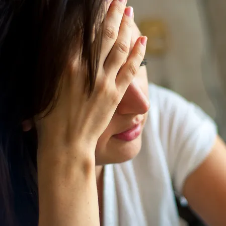 A person wearing a white short-sleeve shirt is resting an arm on a surface. Dark hair is visible on one side.
